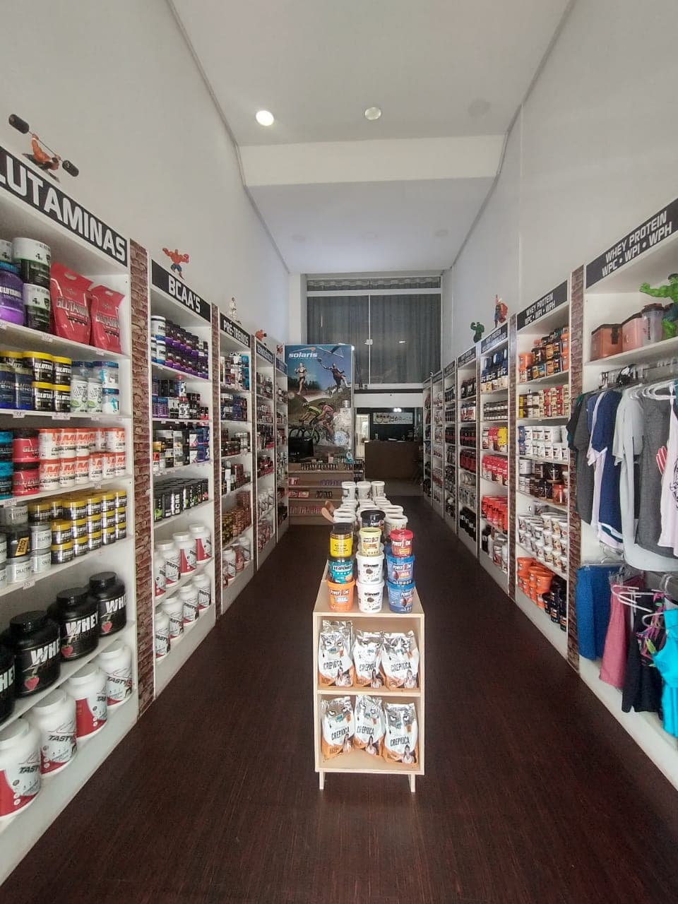 Corredor central da Nutri4Shape com prateleiras de Glutaminas, BCAA e Whey Protein organizadas por categoria